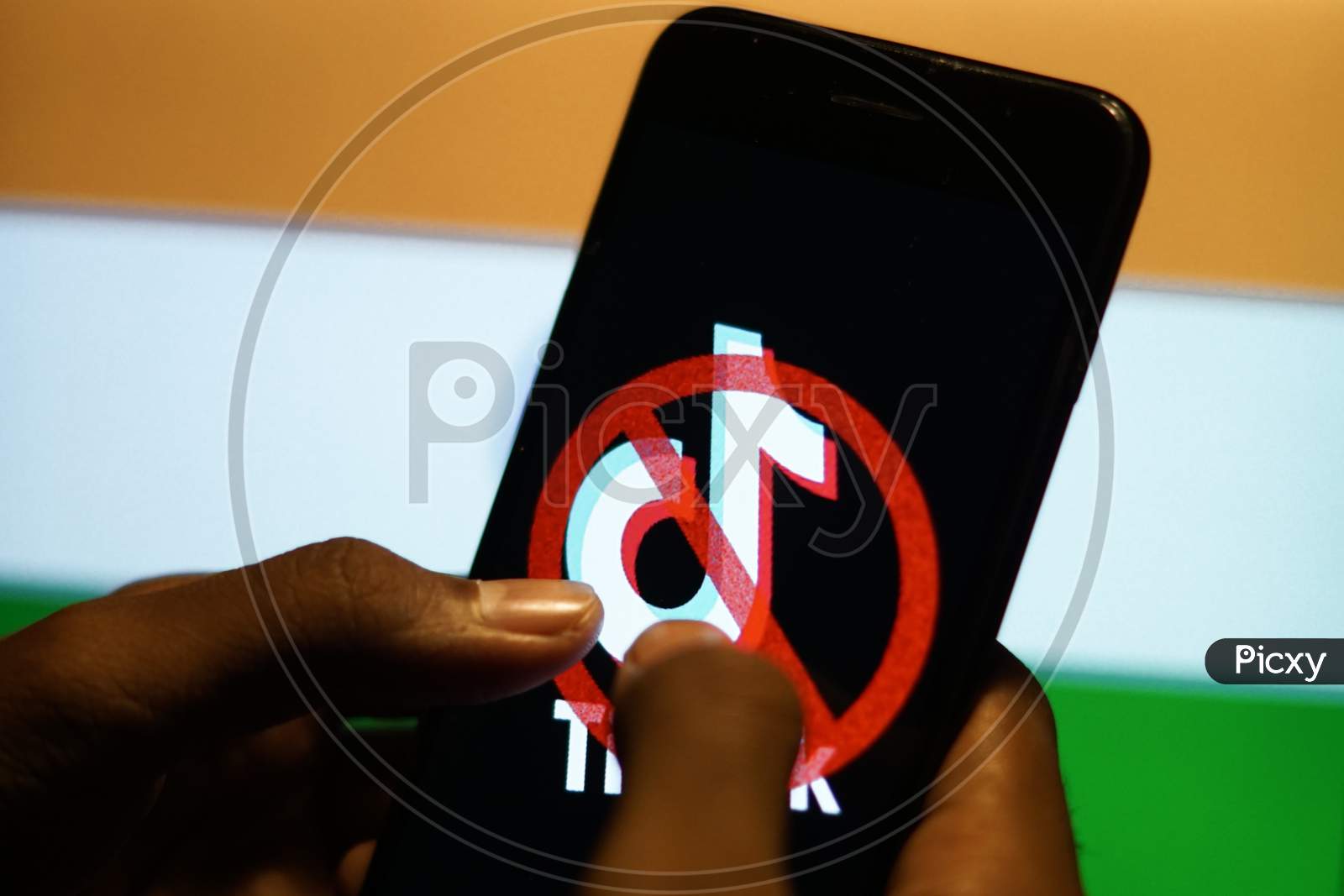 Banned Tiktok Application Logo On A Mobile Screen and fingers about to touch with Indian Flag in the background