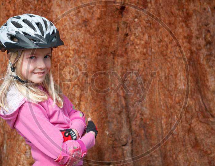 A Young Blonde Girl Poses In A Cycle Helmet And Elbow Pads