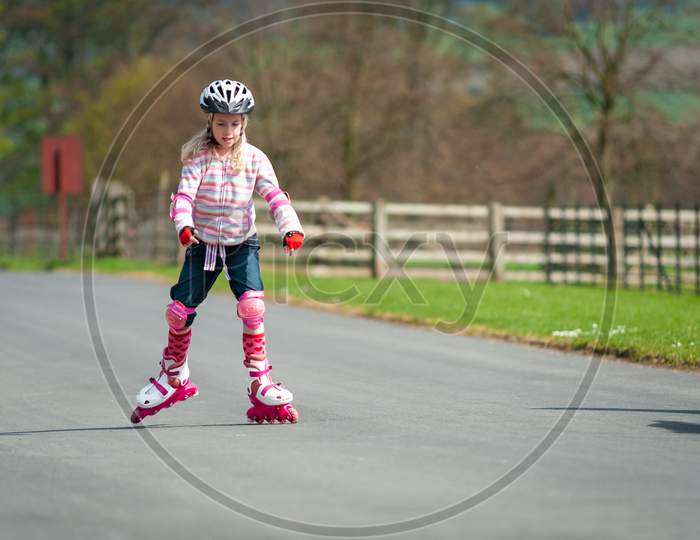 A Young Girl On Roller Blades And Wearing Protective Equipment Skates Along A Country Road