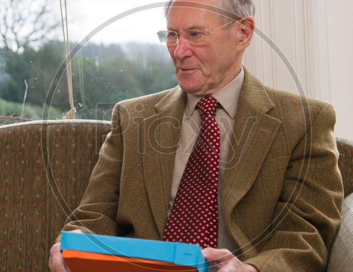 A Well Dressed Elderly Man Unwrapping A Present