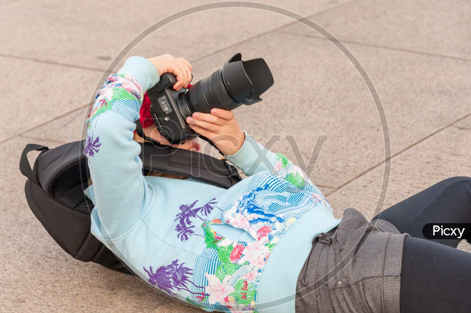 A Very Young Female Photographer Lays On Her Back While Using A Large Dslr Camera To Get The Perfect Angle