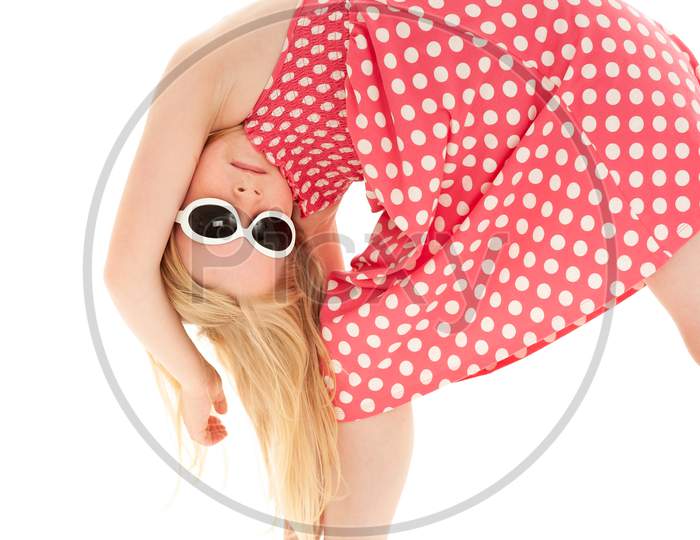 Close Up Of Beautiful Young Blonde Girl Bent Over Doing Stretches And Wearing A Pink And White Polka Dot Dress And Classy White Framed Sunglasses. Isolated On White Studio Background