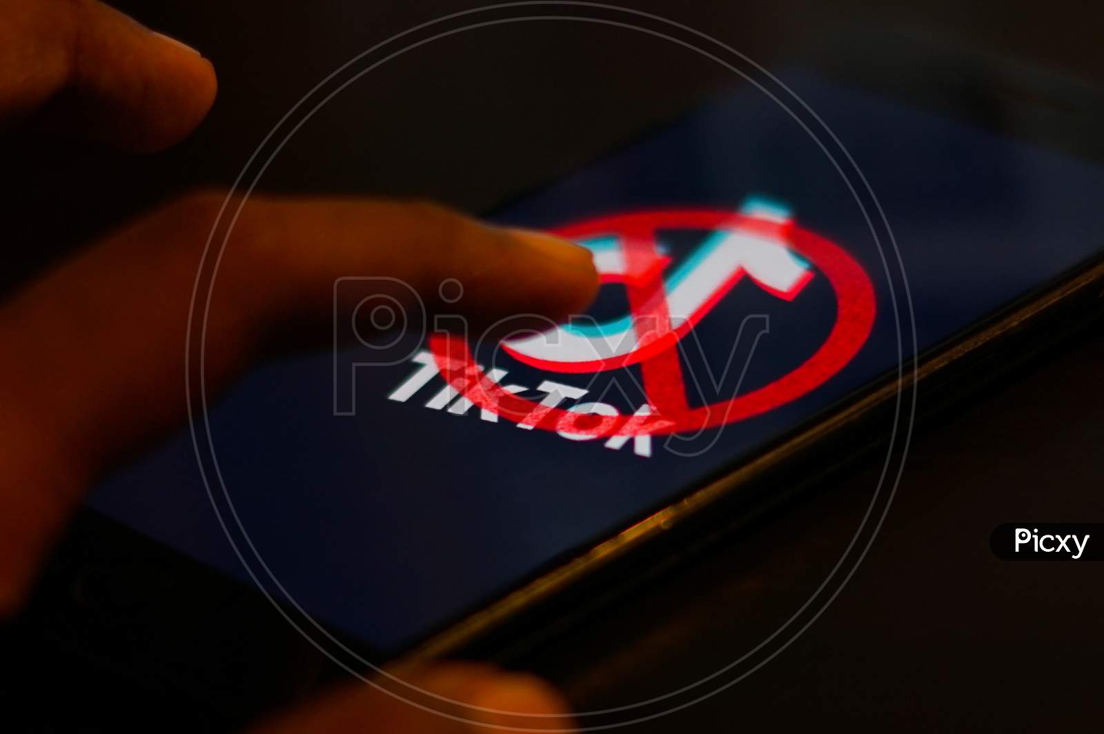 Tiktok Application Logo with banned symbol on a Mobile Screen and a finger about to touch.