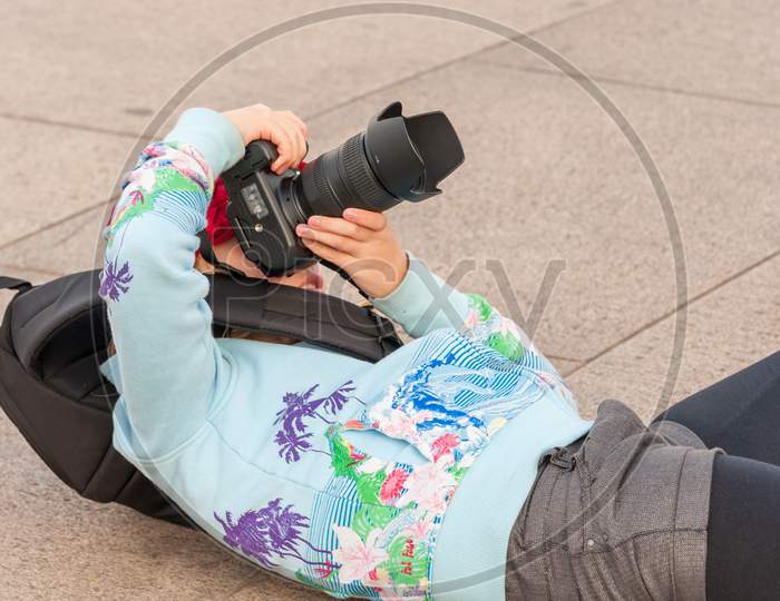 A Very Young Female Photographer Lays On Her Back While Using A Large Dslr Camera To Get The Perfect Angle