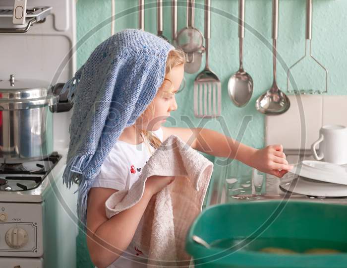 A Young Girl Drying Dishes At A Kitchen Sink