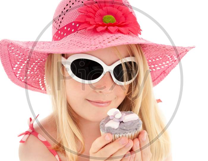 Beautiful Young Blonde Girl In Big Pink Floppy Hat And White Framed Sunglasses Looking At A Cup Cake. White Studio Background