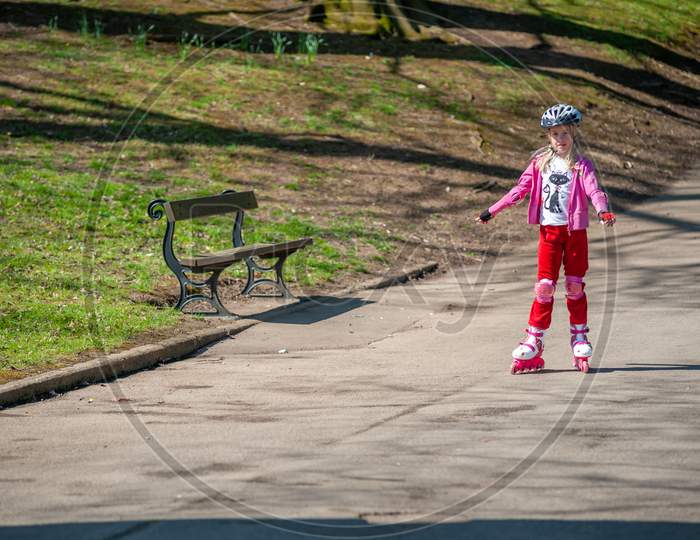 A Young Girl On Roller Blades Passes A Park Bench