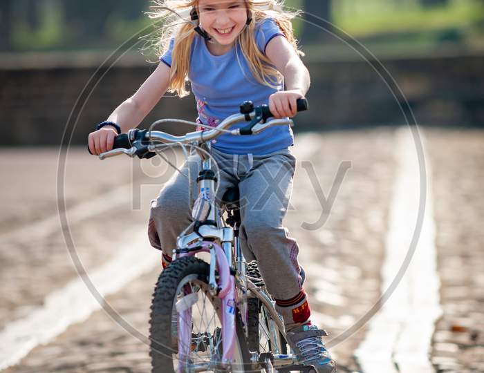 A Very Happy Young Blonde Girl Rides A Bike Along A Cobbled Path