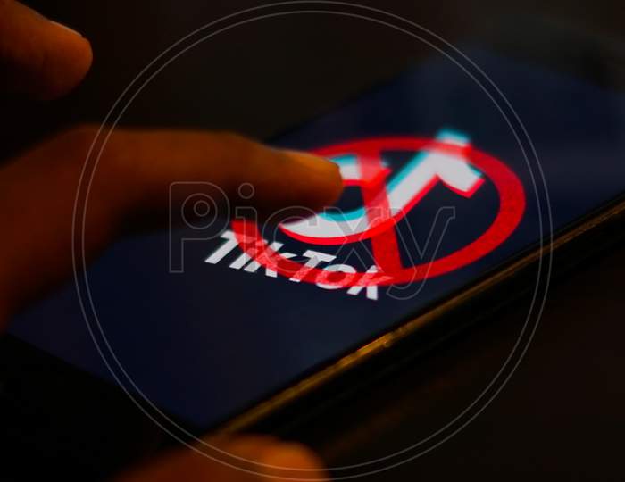 Tiktok Application Logo with banned symbol on a Mobile Screen and a finger about to touch.