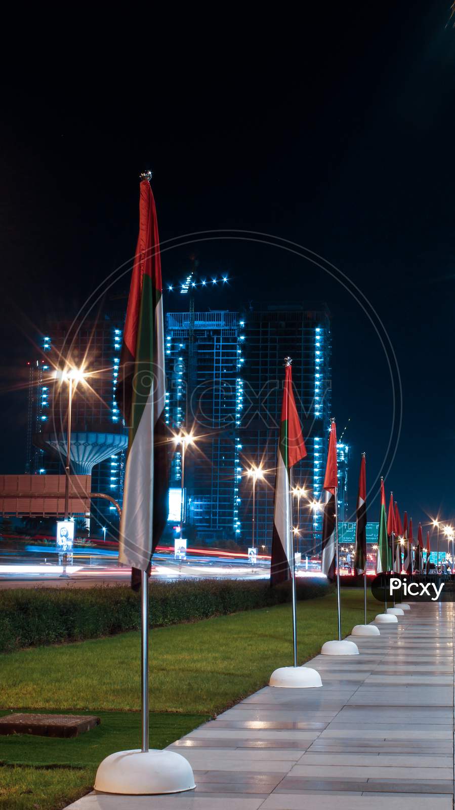 A Long Exposure Photo Of UAE Flags Alongside A Road And Garden In Downtown Dubai, United Arab Emirates.