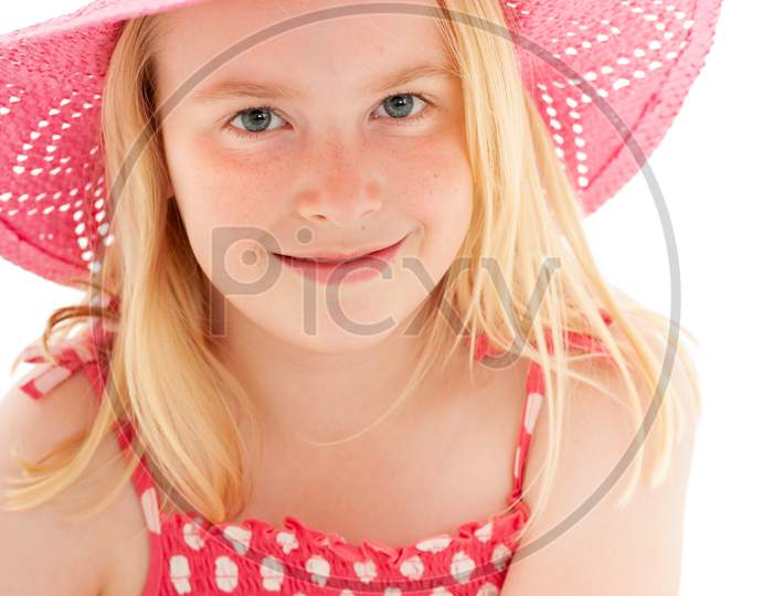Close Up Of Beautiful Young Blonde Girl With Enigmatic Smile Wearing A Big Pink Floppy Hat And Looking Directly At The Camera. Isolated On White Studio Background