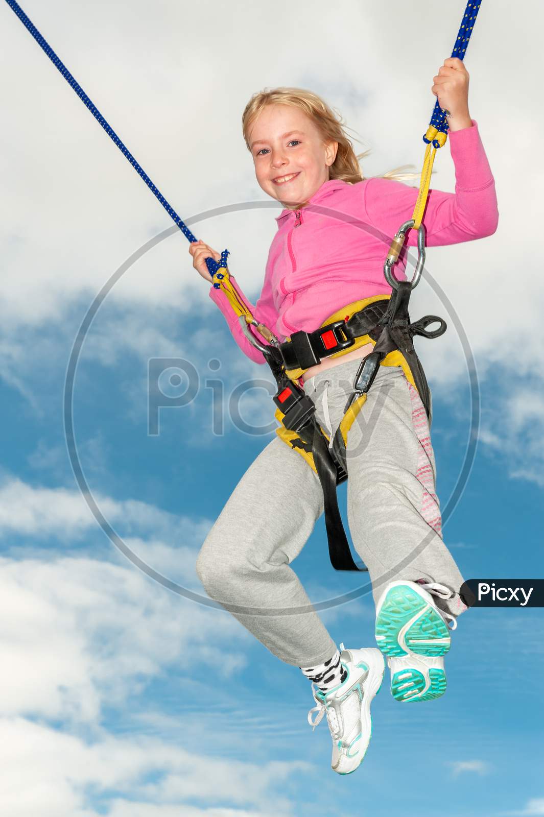 A Happy Young Blonde Girl Bouncing While Attached To Bungee Cords