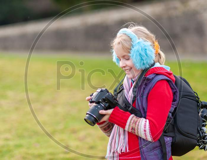 A Happy Young Girl Holding A Camera And Wearing Blue Ear Muffs