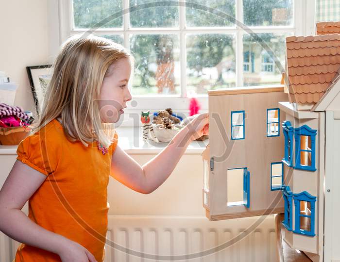 A Young Blonde Girl Opens A Dolls House And Looks Inside