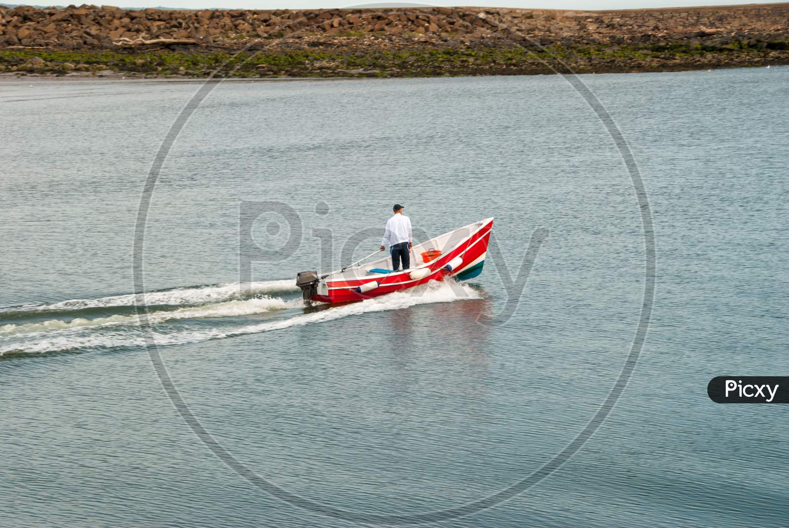 A Man Standing In A Moving Small Red Motorboat On A Calm Day
