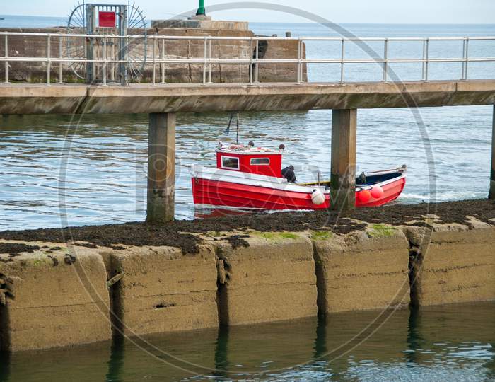 A Small Red Fishing Boat Passes A Pier On A Calm Day