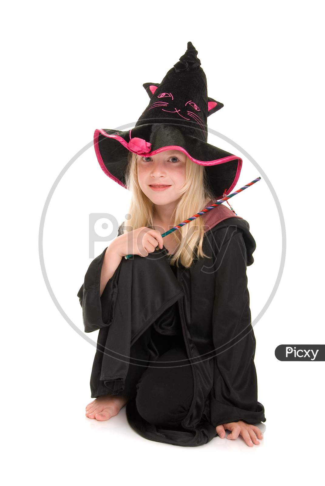 Happy Young Blonde Girl Dressed In A Witches Hat And Cloak, Holding A Wand