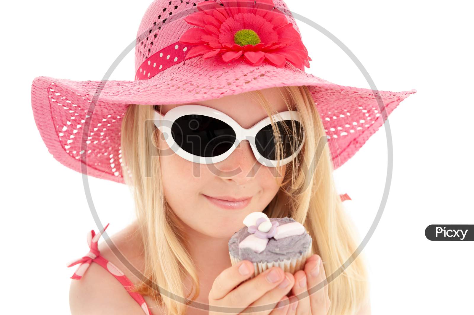 Beautiful Young Blonde Girl In Big Pink Floppy Hat And White Framed Sunglasses Looking At A Cup Cake. White Studio Background