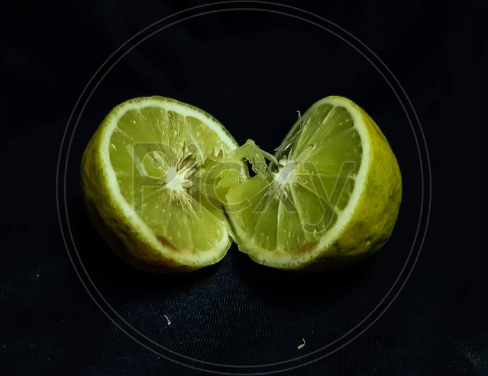 A Lemon Is Cut In The Middle And Placed On A Black Background.