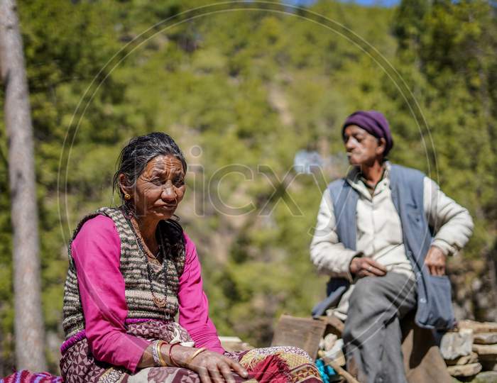 Almora, Uttrakhand / India- June 4 2020: A Photo Of An Old Aged Couple Sitting In A Forest, Man Being Out Of Focus, Old Woman Is In Focus While Seeing Into The Camera.