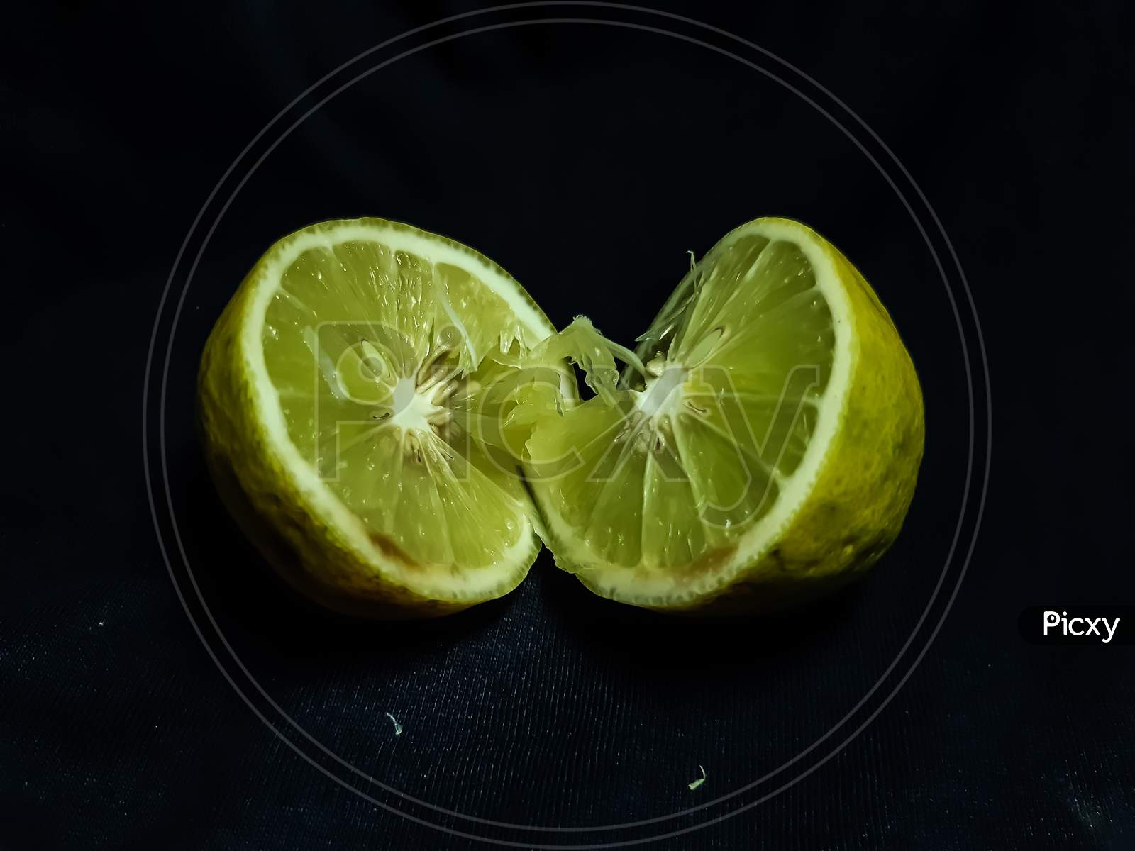 A Lemon Is Cut In The Middle And Placed On A Black Background.