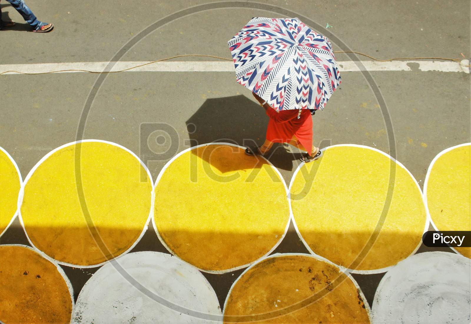 A woman with an umbrella walks past yellow circles painted for physical distancing at a residential-cum-market area, in Mumbai, India on June 29, 2020.