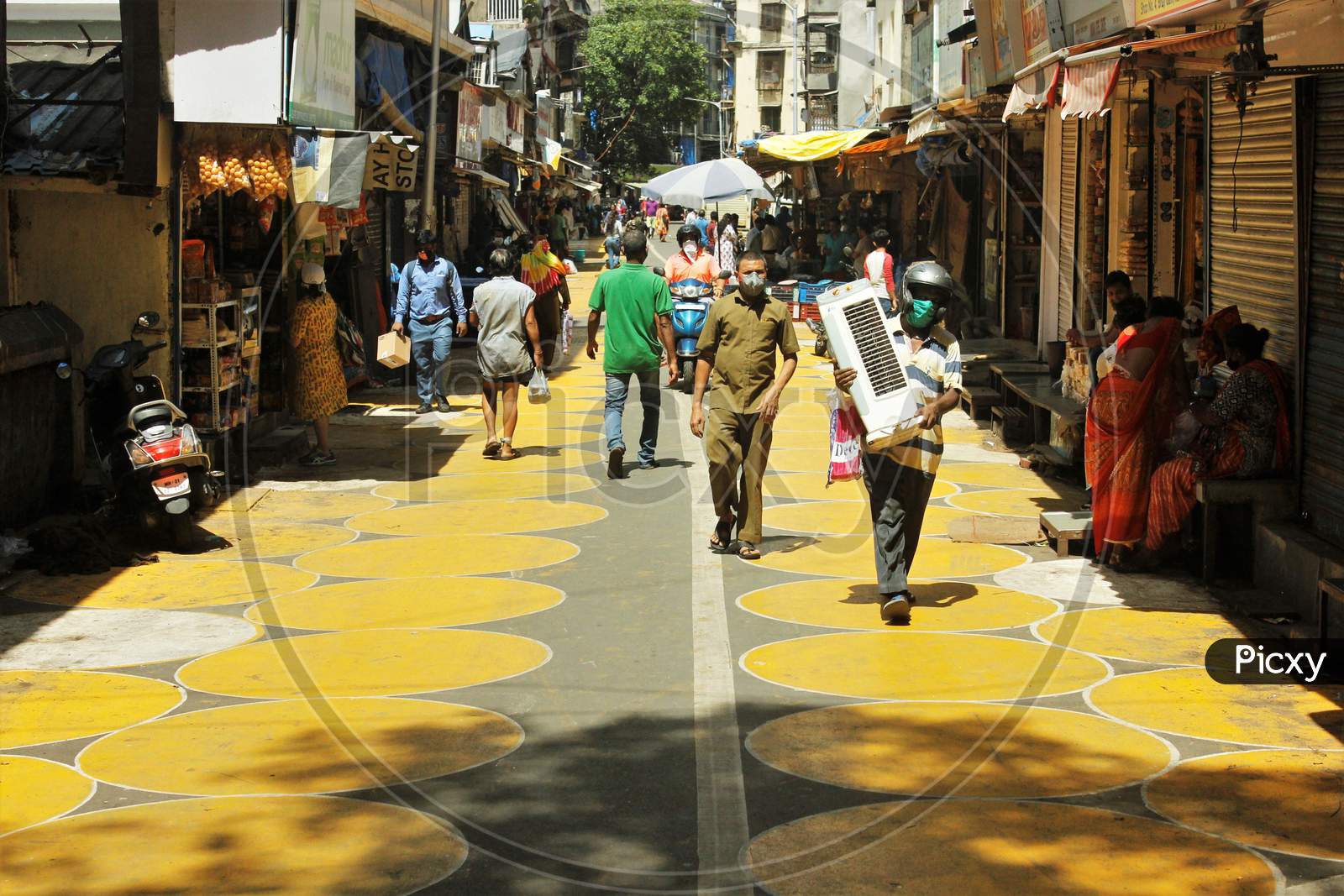 People walk on yellow circles painted for physical distancing at a residential-cum-market area, in Mumbai, India on June 29, 2020.