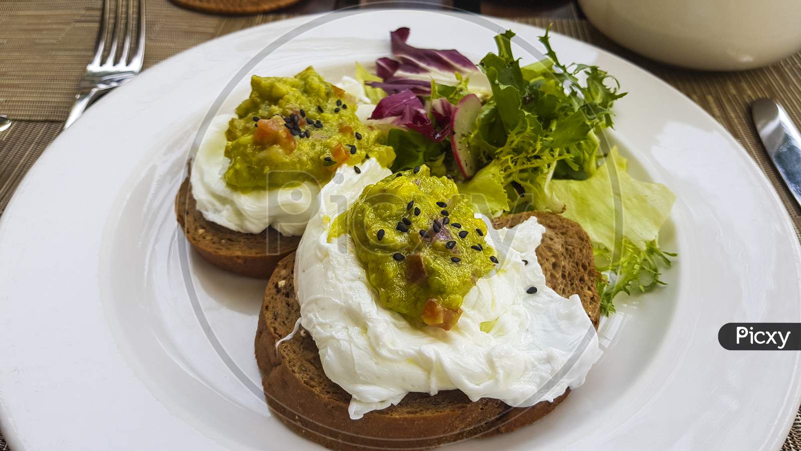 Two Slices Of Dark Bread With Poached Eggs On A White Plate.