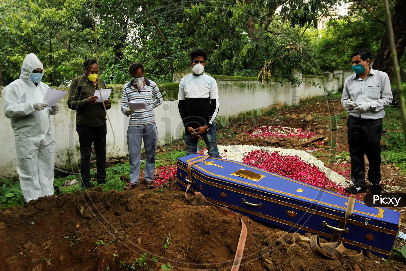 A priest wearing personal protective equipment (PPE) and the relatives pray over the coffin of a person who died from the coronavirus disease (COVID-19) during a funeral at a cemetery in Mumbai, India June 27, 2020.