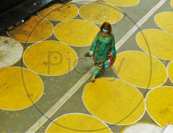 A woman walks past yellow circles painted for physical distancing at a residential-cum-market area, in Mumbai, India on June 29, 2020.
