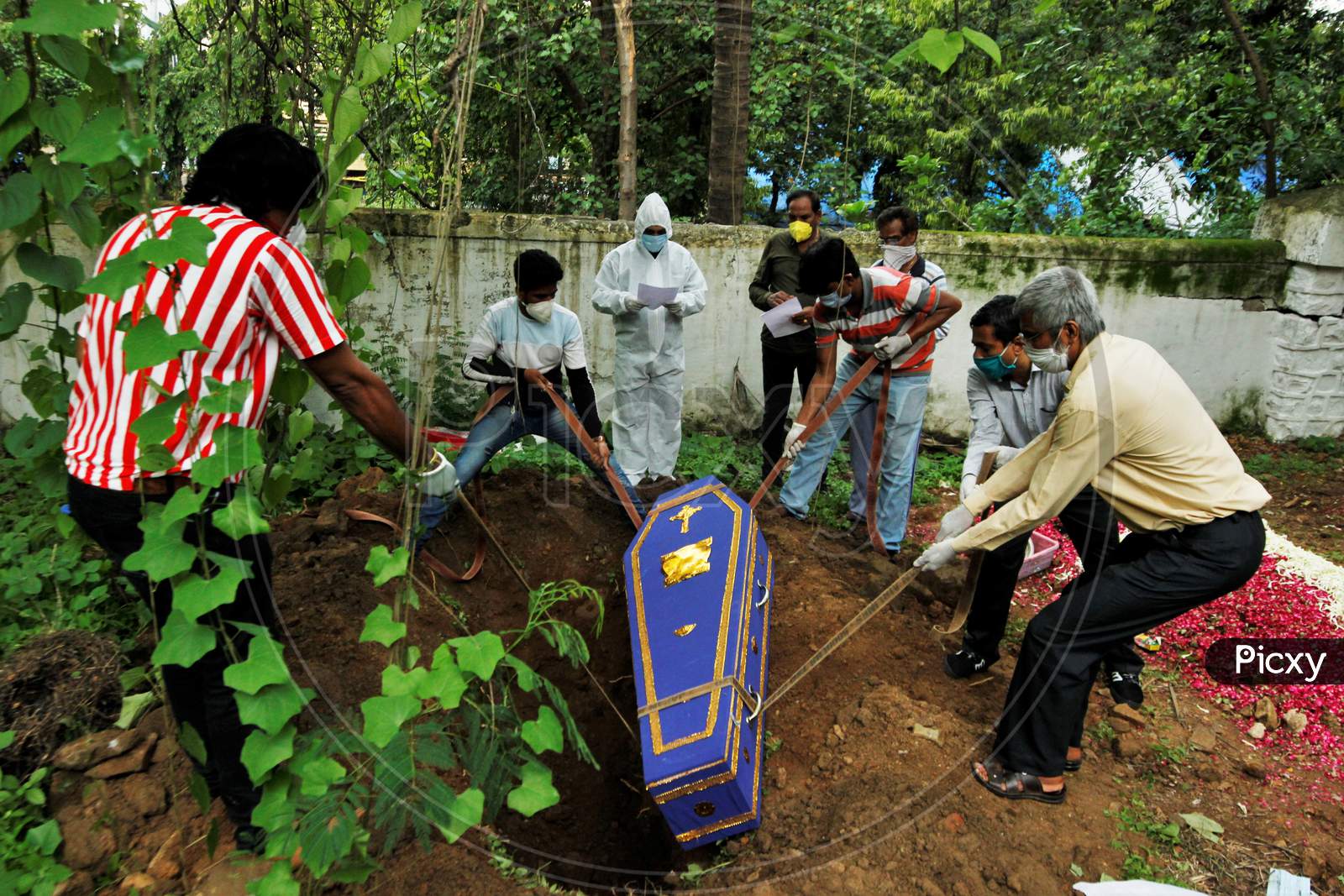 People lower the coffin of a victim who died from the coronavirus disease (COVID-19) into a grave at a cemetery as a priest wearing personal protective equipment (PPE) and relatives watch, during a funeral in Mumbai, India, June 27, 2020.
