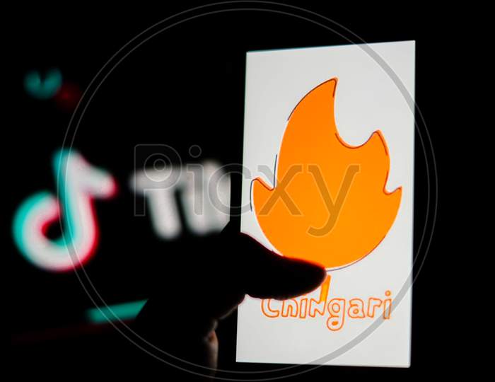 Chingari App logo on Mobile screen with Banned Tiktok Application Logo in the background and a finger about to touch