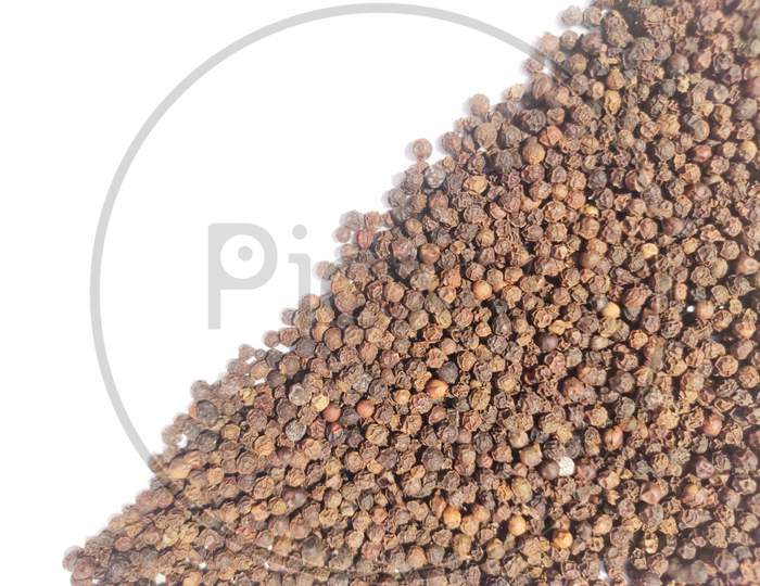 Dry Black peppercorns heap on white background angular top view .