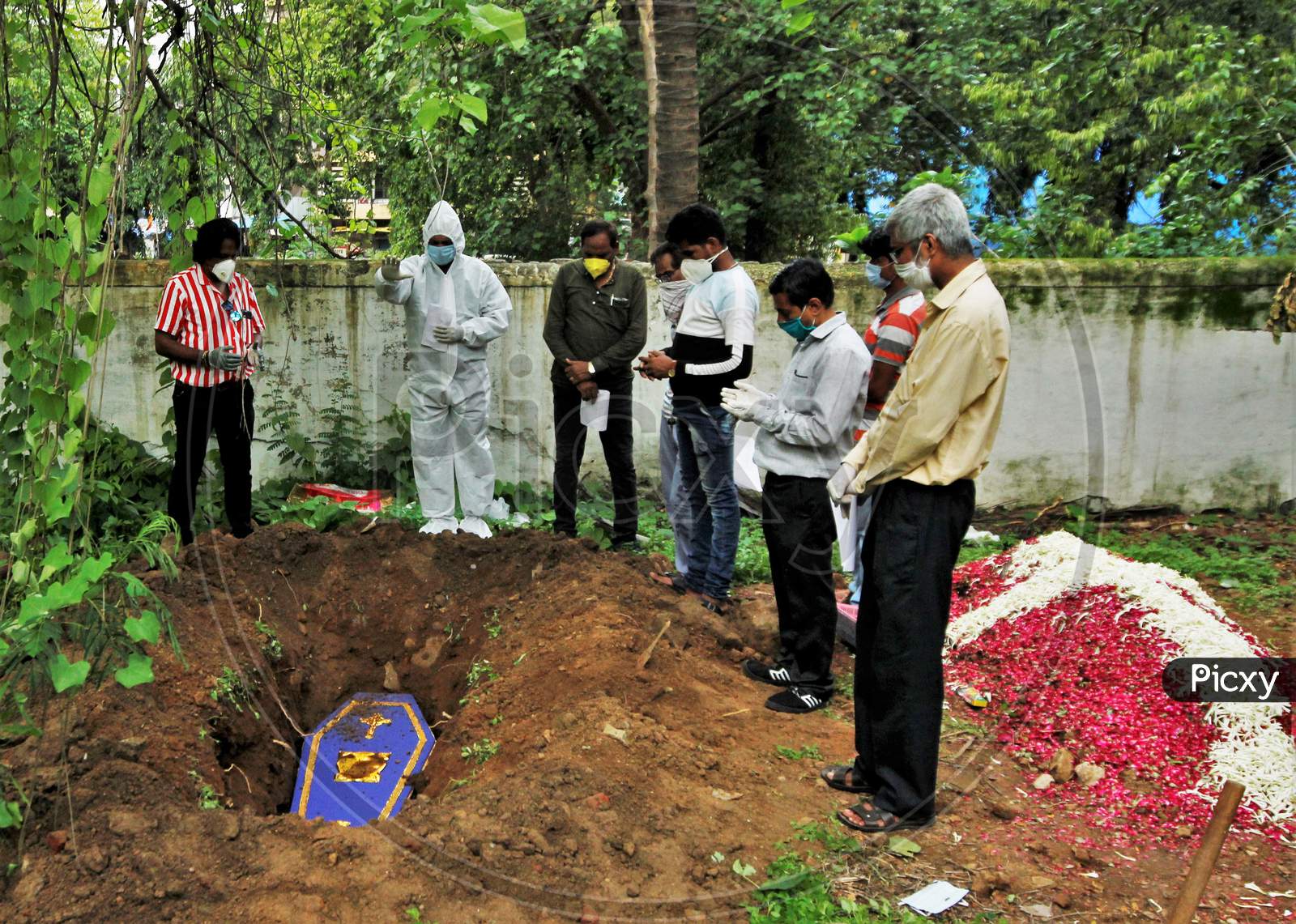 A priest wearing personal protective equipment (PPE) and the relatives pray over the coffin of a person who died from the coronavirus disease (COVID-19) during a funeral at a cemetery in Mumbai, India June 27, 2020.