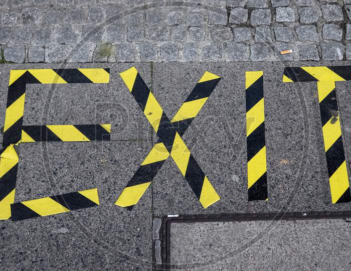 The Word Exit Written With Yellow And Black Barrier Tape Onto A Sidewalk.