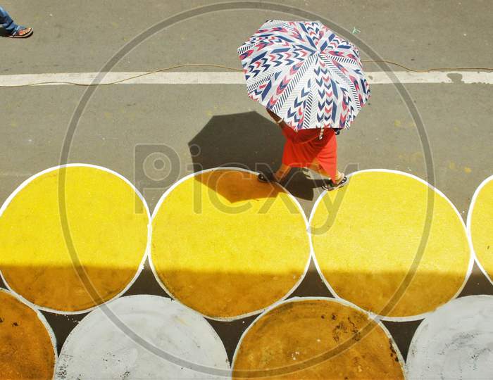 A woman with an umbrella walks past yellow circles painted for physical distancing at a residential-cum-market area, in Mumbai, India on June 29, 2020.