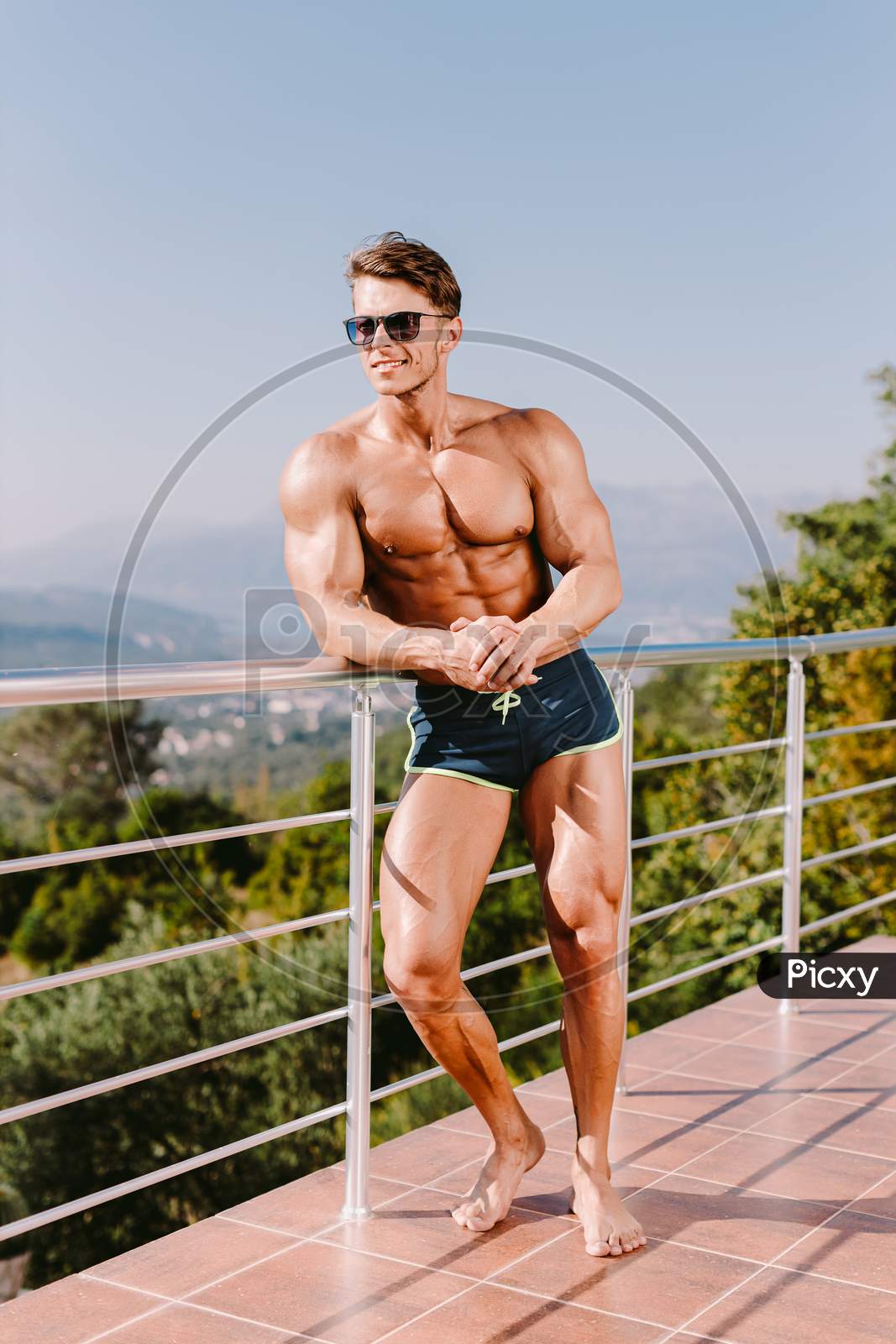 Photogenic Muscular Man Smiling And Posing Naked Torso In Swim Trunks And Sunglasses