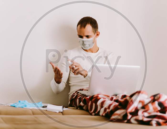 Caucasian Man Wearing Face Mask Using Hand Sanitizer And Working At Home.