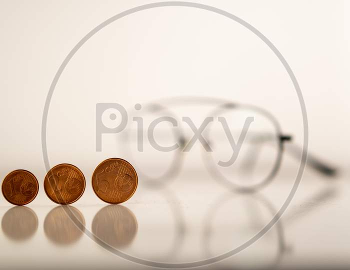 European cents (Coins) and a spectacle against a white background to highlight the collapsed World economy (Global recession) during Covid-19 (Coronavirus) pandemic through the vision of economists.