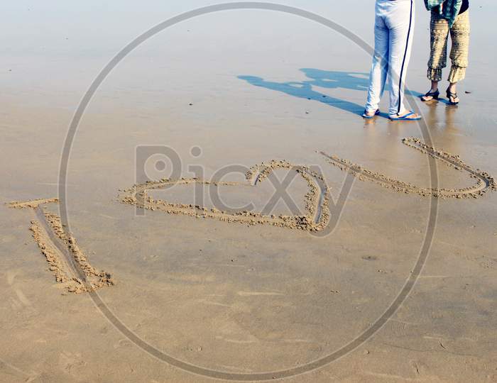I Love You written on a Beach Shore with People moving in the Background