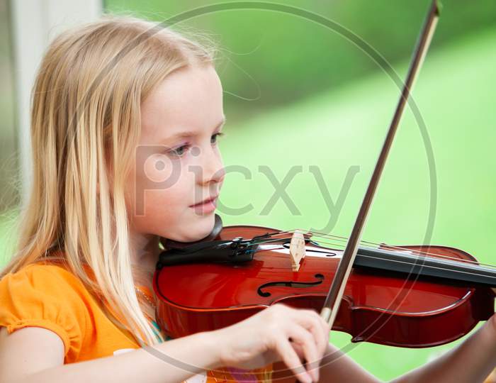 Pretty Blonde Little Girl Playing Violin With A Blurry Green Background