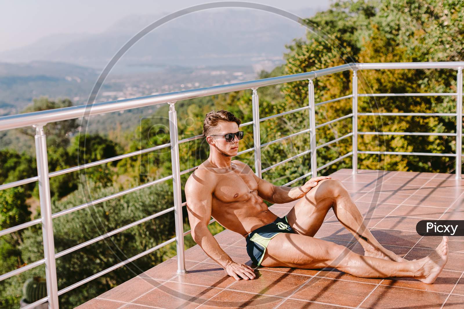 Fashion Portrait Of A Muscular Man Posing Shirtless In Swim Trunks And Sunglasses