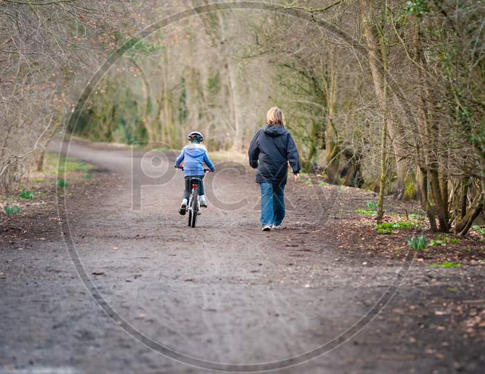 Young Girl Riding Bike Next To Mum Along Country Path