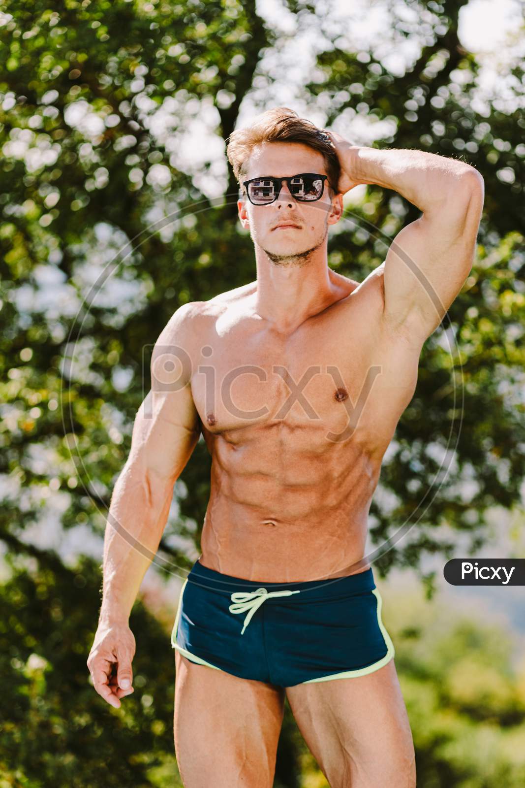 Portrait Of A Muscular Man In Swim Trunks And Sunglasses