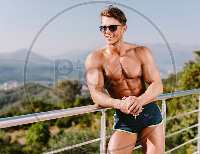 Attractive Muscular Man Smiling And Posing In Swim Trunks Outdoors