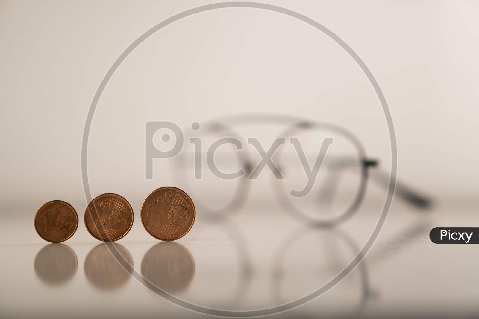 European cents (Coins) and a spectacle against a white background to highlight the collapsed World economy (Global recession) during Covid-19 (Coronavirus) pandemic through the vision of economists.