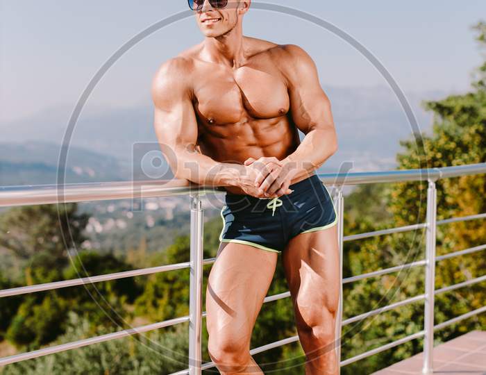 Photogenic Muscular Man Smiling And Posing Naked Torso In Swim Trunks And Sunglasses