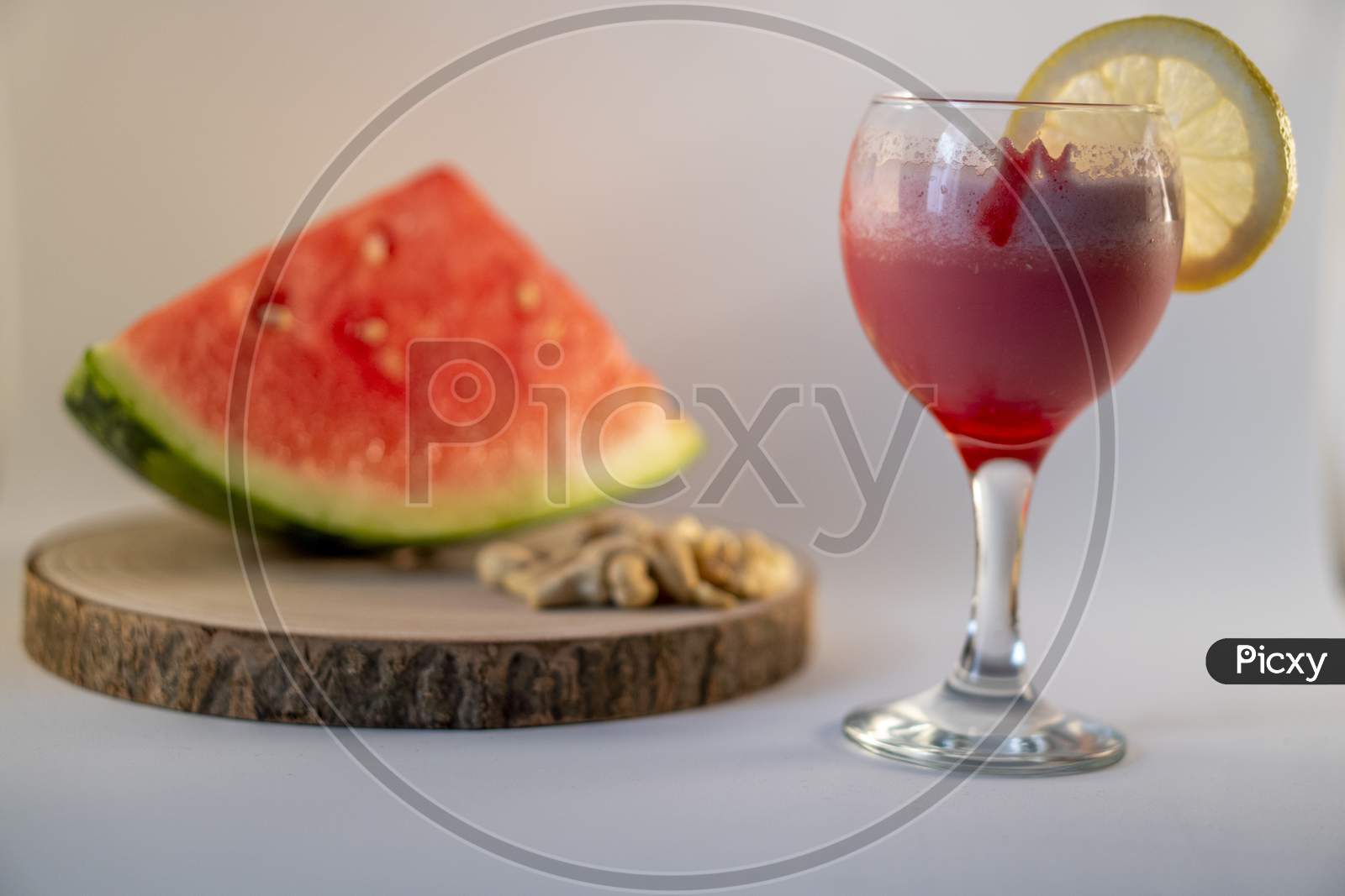 Fresh watermelon juice with a lemon slice, a watermelon piece and Cashew nuts on a white background.