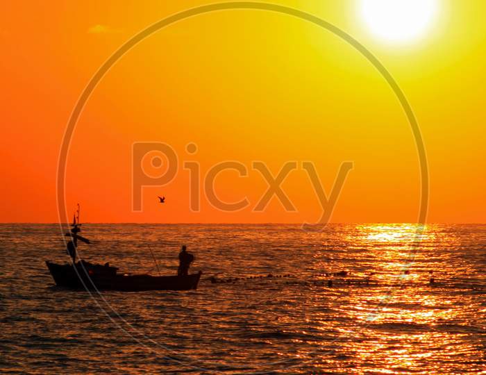 Fisherman In Boat On The Sea Before Sunset