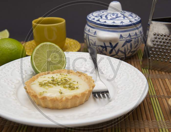 Side View Of Lemon Tart On Dish Plate With Lemon Slices On Table.